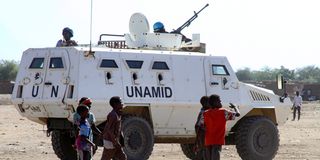 Children walk past a vehicle of the United Nations and African Union peacekeeping mission in South Darfur in December 2020.