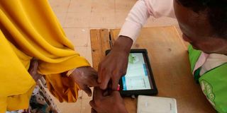 A polling clerk uses a Kiems kit to identify a voter.