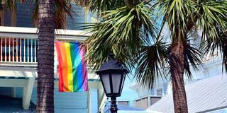 A balcony in Key West, Florida, displays a gay pride flag, with palm trees and a street lamp