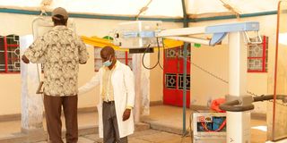 A medic helps a resident onto the platform of a digital x-ray machine during a Tuberculosis screening drive in Kisumu County