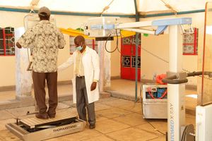 A medic helps a resident onto the platform of a digital x-ray machine during a Tuberculosis screening drive in Kisumu County