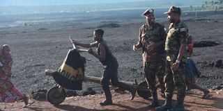 A Congolese man pushes a cart past  KDF soldiers