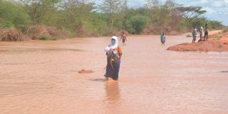 A woman with a child wades through a flooded Bura-Garisa highway.