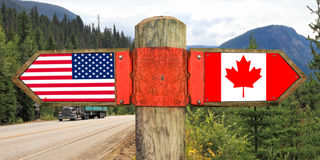 Wooden signpost with two arrows - American and Canadian national flags 