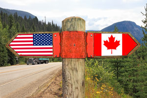 Wooden signpost with two arrows - American and Canadian national flags 