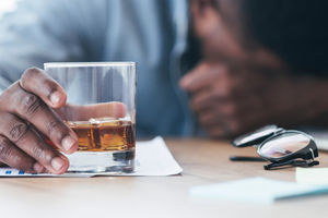 Drunk black employee sleeping at workplace, holding glass with alcohol