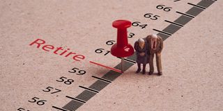 Miniature figure couple Senior Pensioners standing with red pin on ruler