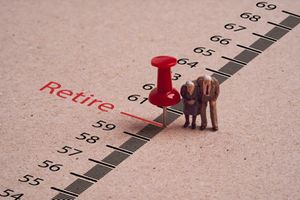 Miniature figure couple Senior Pensioners standing with red pin on ruler