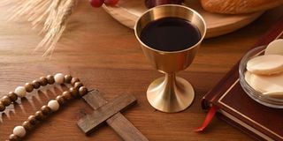 Wine glass and consecrated hosts on wooden table with christian cross 