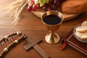 Wine glass and consecrated hosts on wooden table with christian cross 