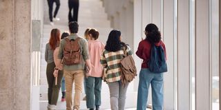 Back view of university students walking through hallway while going on a lecture