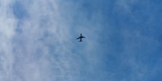 A distant airplane flying across a calm blue sky with thin clouds