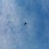 A distant airplane flying across a calm blue sky with thin clouds