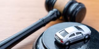 A judge gavel and a miniature car on a wooden table.